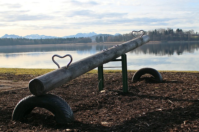A metal seesaw by a lake with mountains in the background.