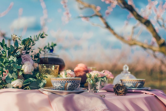 Fancy tea cups and flowers on a pink table cloth against a lovely natural scene