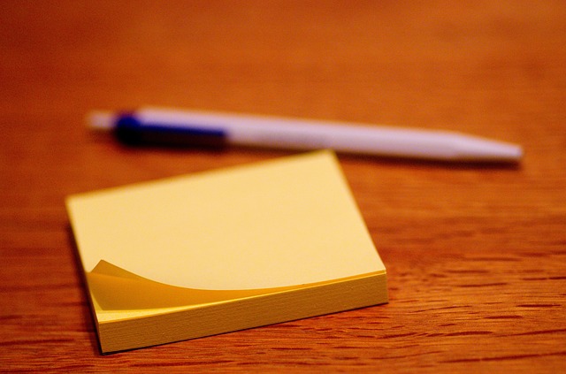 Close up of a stack of yellow post-it notes and a blurred pen in the background.